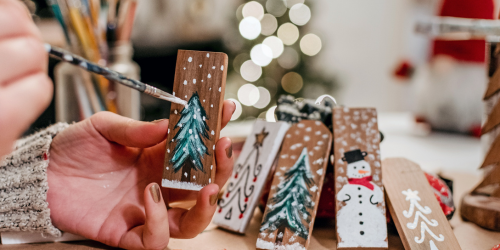 person hand painting christmas trees on wooden blocks